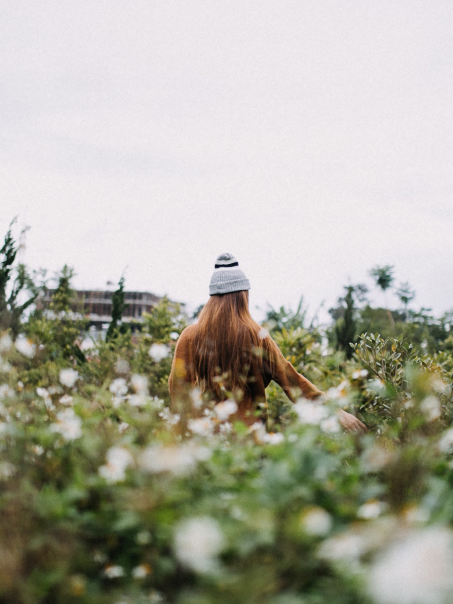 jeune femme rousse au style hispter avec un bonnet qui se promène dans un champ pour préparer les cultures de février